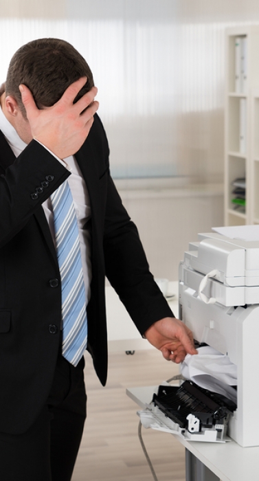 Irritated businessman looking at paper stuck in printer at office