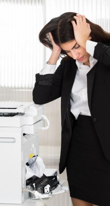 Irritated young businesswoman looking at paper stuck in printer at office
